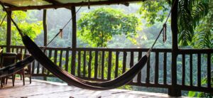 Eine Hängematte, aufgespannt auf einem Balkon vor hohen Bäumen im Wald.