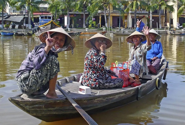 In einem Holzboot auf einem Fluss sitzen 4 asiatische Frauen mit Einkäufen und winken freundlich
