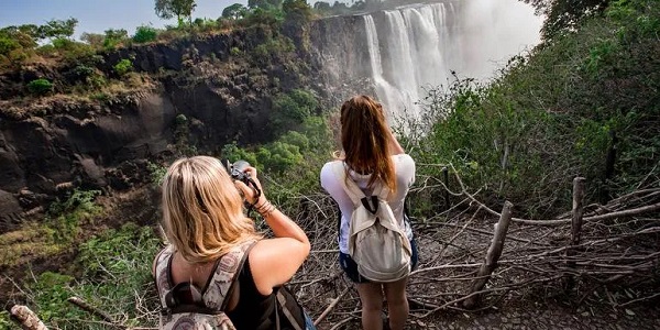 Zwei Personen stehen im Wald und machen Fotos von einem Wasserfall