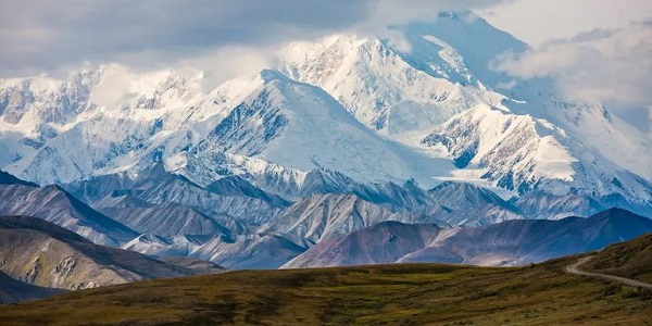 Panoramaaufnahme einer verschneiten Berglandschaft im Hintergrund, davor eine grüne Grasfläche
