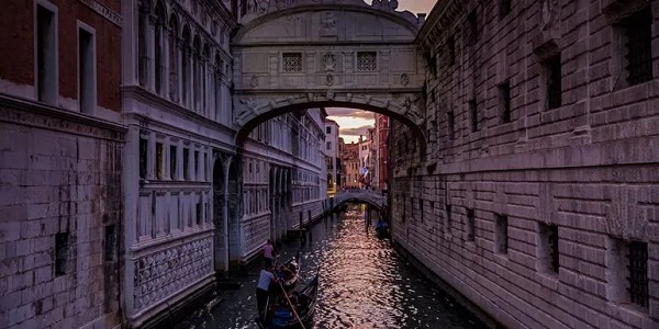 Ein kleines Boot führt durch einen durch eine Stadt verlaufenden Kanal mit mehreren Brücken darüber