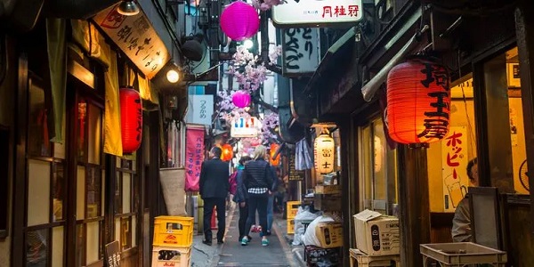 Eine enge Gasse in einer japanischen Stadt, an deren Ende einige Menschen stehen